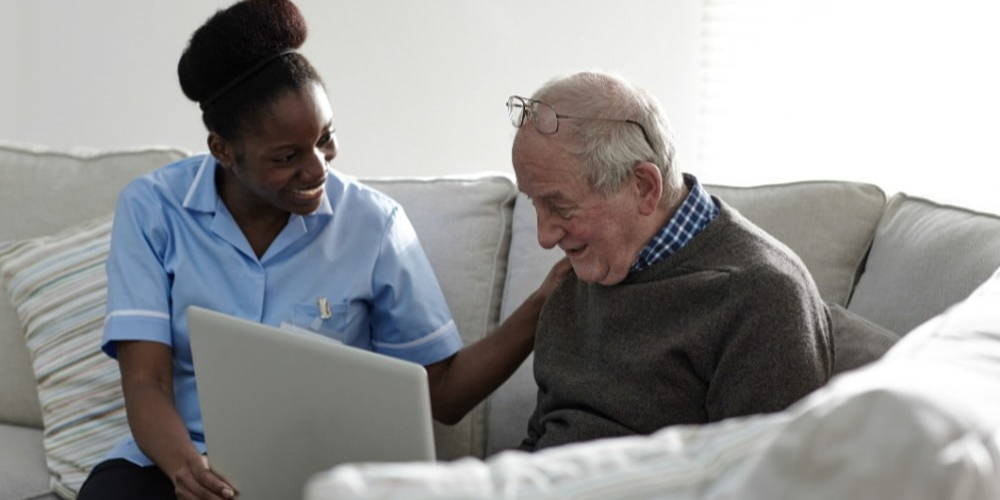 telehealth assistant assisting elderly home care client with computer